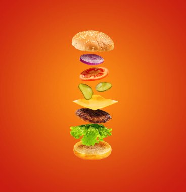 Turuncu arka planda uçan malzemeli hamburger. Havada lezzetli bir hamburger var. Yiyecek uçurma konsepti.