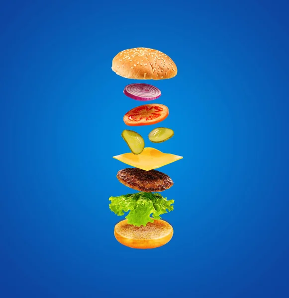 Burger with flying ingredients on blue background. Delicious hamburger in the air. Food levitation concept.