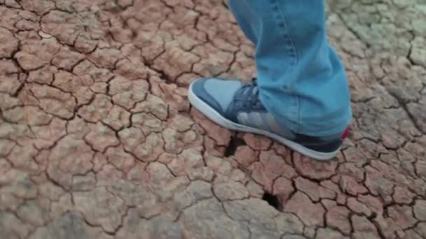 Primer plano de un hombre pie en pantalones vaqueros azules hasta la colina en la tierra agrietada seca la foto fue tomada en modo de cámara lenta — Vídeos de Stock