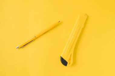 Sarı arka planda sarı kalem ve ofis bıçağı. Üst Manzara. Minimalizm. Geçmişi temiz görünüyor. Düz yatıyordu. Kopyalama alanı ile şablon. İki nesne. Konsept başbakanlık, ofis malzemeleri, aksesuarlar