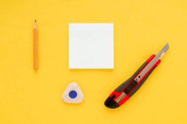 Beyaz kare notlar, kalem, silgi, kırmızı ofis bıçağı ve sarı kağıtta keskinleştirici.