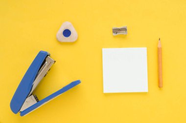 Beyaz kare notlar, kalem, silgi, mavi zımba, sarı kağıtta keskinleştirici.