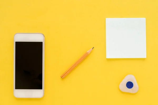 White square notes, pencil, eraser, white smartphone and sharpener on yellow paper background