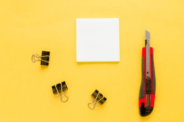 Beyaz kare notlar, kırmızı ofis bıçağı, sarı arkaplanda fotokopi alanı olan buldog kağıdı. Model yap. Üst Manzara. Konsept başbakanlık, ofis malzemeleri, aksesuarlar