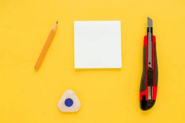 White square notes, pencil, eraser, red office knife and sharpener on yellow paper background