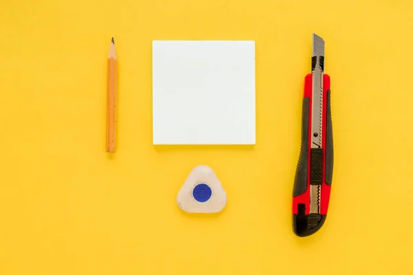 White square notes, pencil, eraser, red office knife and sharpener on yellow paper background