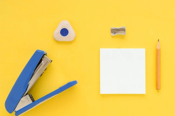 White square notes, pencil, eraser, blue stapler, sharpener on yellow paper backgroun