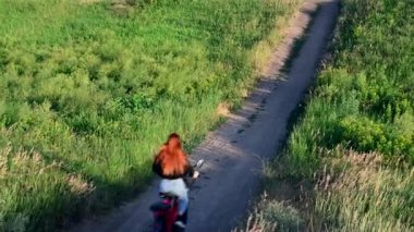 Beyaz kız, güneşli bir yaz gününde toprak yolda kırmızı elektro bisikletini sürüyor. Arkadan bak. Fitness, spor, insanlar sağlıklı yaşam tarzı konsepti
