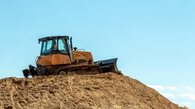 Mavi gökyüzüne karşı büyük bir kum yığını üzerinde sarı buldozer
