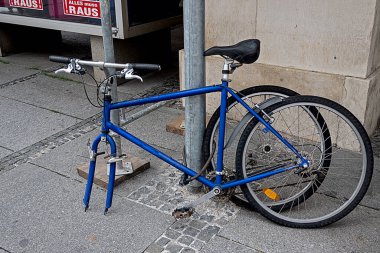 Lastiği sökülmüş, lağıma zincirlenmiş mavi bisiklet.