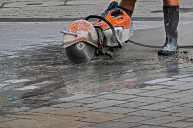 Sokakta elinde elektrikli makasla lastik çizmelerle çalışan bir adam.