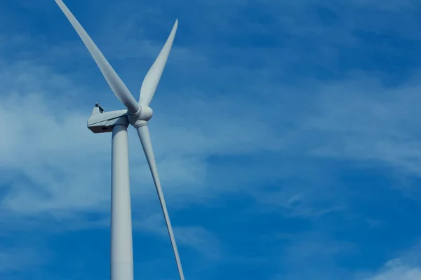 Close upward view of the rotor blades on a giant wind power turbine, with blue sky background