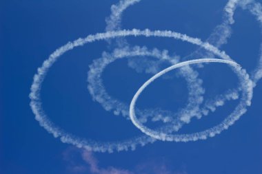 Abstract low angle view of airplane skywriting in a circular pattern, with deep blue sky background