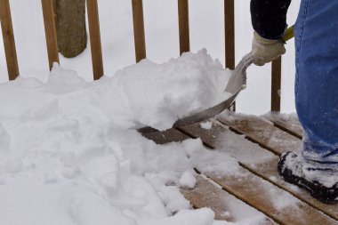 Close up view of an unidentifiable person shoveling heavy snow off a wooden deck floor in winter