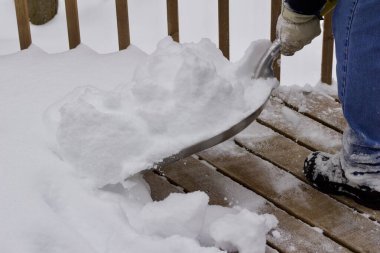 Close up view of an unidentifiable person shoveling heavy snow off a wooden deck floor in winter
