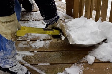 Close up view of an unidentifiable person shoveling heavy snow off a wooden deck floor in winter
