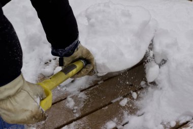 Close up view of an unidentifiable person shoveling heavy snow off a wooden deck floor in winter