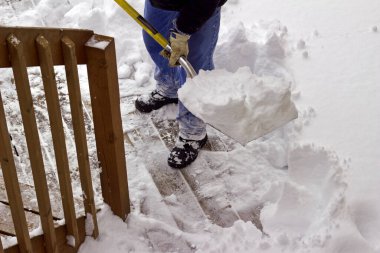 Close up view of an unidentifiable adult man shoveling heavy snow off a wooden deck floor in winter
