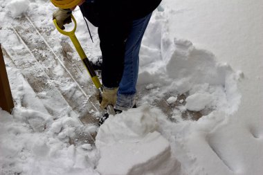 Close up view of an unidentifiable person shoveling heavy snow off a wooden deck floor in winter