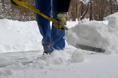 Close up view of an unidentifiable person shoveling heavy snow off a wooden deck floor in winter