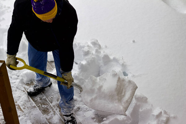 Close up view of an unidentifiable person shoveling heavy snow off a wooden deck floor in winter