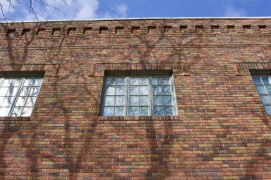 Tuğla duvar dokusu arkaplan ile güzel toprak tonlu tuğlalar kahverengi, kırmızı ve yeşil tonlarda, modern cam blok pencere ve düşük açılı güneş ışığı ağaç gölgeleri (düşük açı görünümü) göstermektedir)