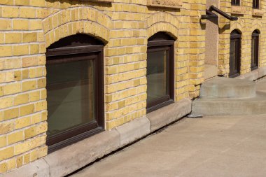 Kaldırımlı sarı tuğlalı bir binanın çekici kemerli pencerelerini kapatın.