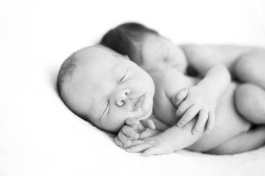 Yeni doğan ikizler kucaklaşarak yatıyorlar. Bebekler battaniyenin üzerinde birlikte yatarlar. Doğuştan kardeş sevgisi. Kız kardeşler, erkek kardeşler. Bebek bakımı. Siyah beyaz resim