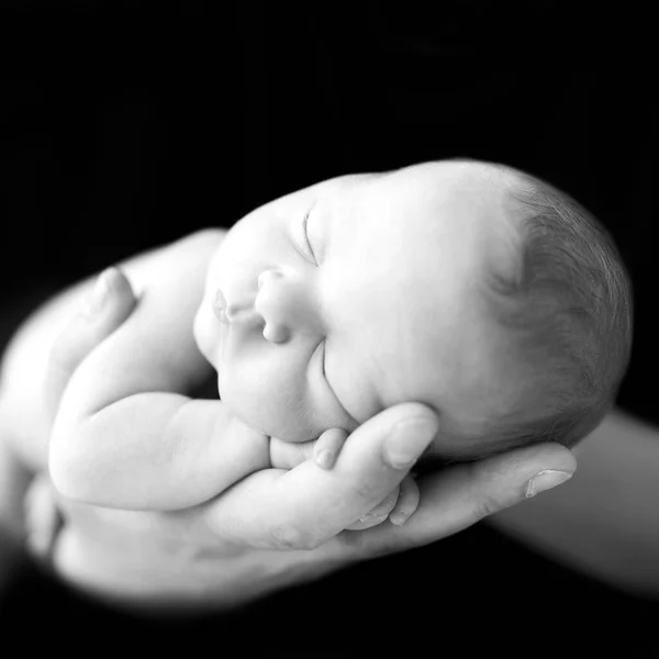 Newborn baby girl or boy sleep on parent hand. Neonatal care. Black and whitepicture. Sleeping infant on black background.