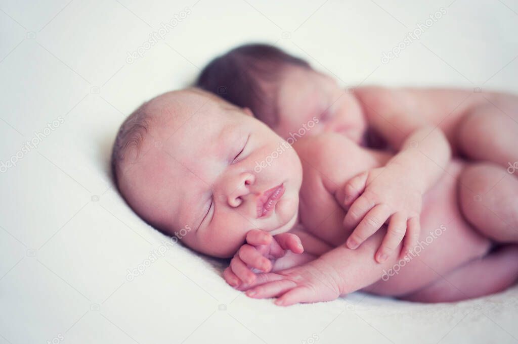 Newborn twins sleeping together in a hug. Babies lies together on blanket. Sibling love from birth - sisters, brothers. Baby care