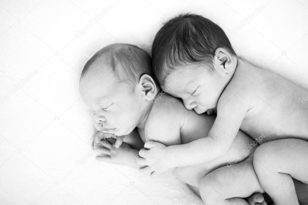 Newborn twins sleeping together in a hug. Babies lies together on blanket. Sibling love from birth - sisters, brothers. Baby care. Black and white picture