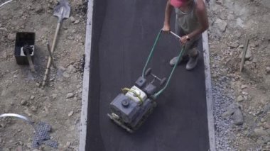 İşçi kaldırımın asfalt kaldırımı için manüel bir silindir itiyor yol kapalı çalışıyor, yukarıdan görünüyor.