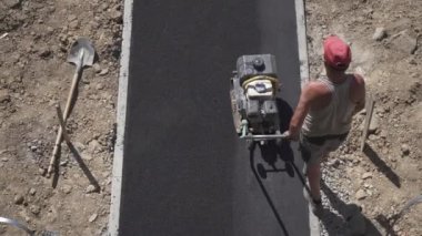 İşçi kaldırımın asfalt kaldırımı için manüel bir silindir itiyor yol kapalı çalışıyor, yukarıdan görünüyor..