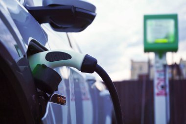 Beyaz elektrikli bir arabaya yakın çekim şarj ediliyor.Altrernative eko enerji yakıtı.Enerji arzı pili şarj etmek için elektrikli arabaya bağlanıyor.Çevre dostu alternatif enerji kavramı