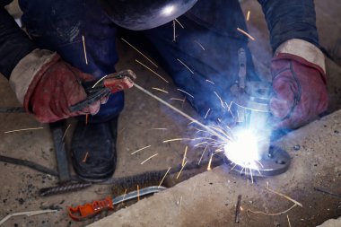 Üretim tesisinde yarı otomatik kaynak makinesinde elektrot ile çalışan kaynakçı. Kaynak kaynaklarından çıkan parlak kıvılcımlar.