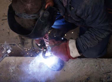 Üretim tesisinde yarı otomatik kaynak makinesinde elektrot ile çalışan kaynakçı. Kaynak kaynaklarından çıkan parlak kıvılcımlar.