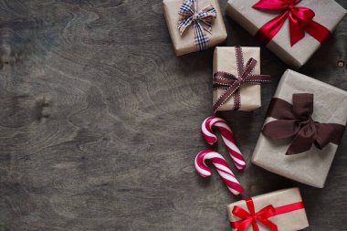 Kahverengi kağıda sarılı, farklı kurdelelerle ve Noel şekerleriyle bağlanmış pek çok hediye kutusu ahşap bir zemin, üst görünüm, kopya alanı üzerine kuruludur. Noel ve yeni yıl kavramı.