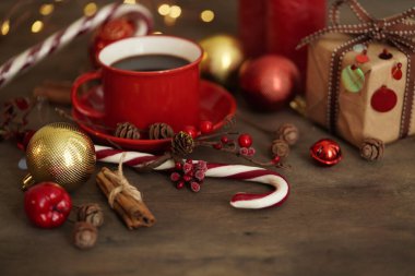Noel süslemeleri. Kahveli kırmızı bardak, hediye kutusu, Noel şekeri, toplar, koniler ve tahta arka planda tarçın, seçici bir odak. Noel ve Yeni Yıl kavramı.