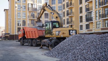Sarı CAT kazıcı yükleyici çakıllı bir inşaat alanında çalışıyor. Bir kamyona çakıl yüklüyorum. Yol inşaatı. Bir otopark inşaatı, Kiev, Ukrayna 09.02.2020.
