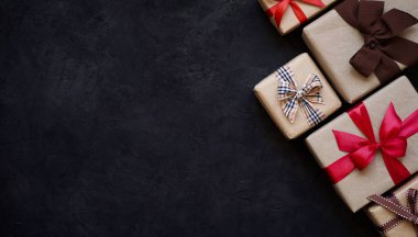 Kahverengi kağıda sarılı ve farklı kurdelelerle bağlanmış birçok hediye kutusu siyah arka plan, üst görüş, kopya alanı. Noel ve yeni yıl kavramı..