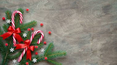 Kırmızı pruvalı Noel lolipopu, beyaz kar taneleri, kırmızı toplar ve kahverengi ahşap arka planda noel ağacı dalı, fotokopi alanı, üst manzara, düz katman. Noel ve yeni yıl dekorasyonu kavramı..