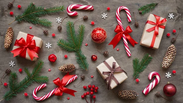 Christmas or new year background,simple composition of christmas decoration gift boxes,red balls,cones, snowflakes,lollipops and fir branches on brown wooden background,flat lay,pattern.