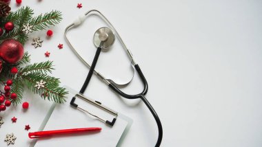 Beyaz arka planda noel bayrağı dalları, koniler, kırmızı toplar, kar taneleri, steteskop ve tablet. Kopyalama. Tıbbın yeni yılı.