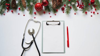 Beyaz arka planda noel bayrağı dalları, koniler, kırmızı toplar, kar taneleri, steteskop ve tablet. Kopyalama. Tıbbın yeni yılı.