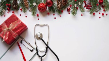 Noel pankartı hediye kutusu, köknar dalları, koniler, kırmızı toplar, kar taneleri, steteskop ve beyaz arka plan manzaralı tablet. Kopyalama. Tıbbın yeni yılı. Doktor metni yazar..