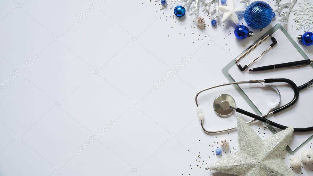 Christmas medical banner christmas decor white stars,blue balls, snowflakes, stethoscope and tablet on white background top view. Copyspace. Medicine new year flatly. Doctor writes down the text.