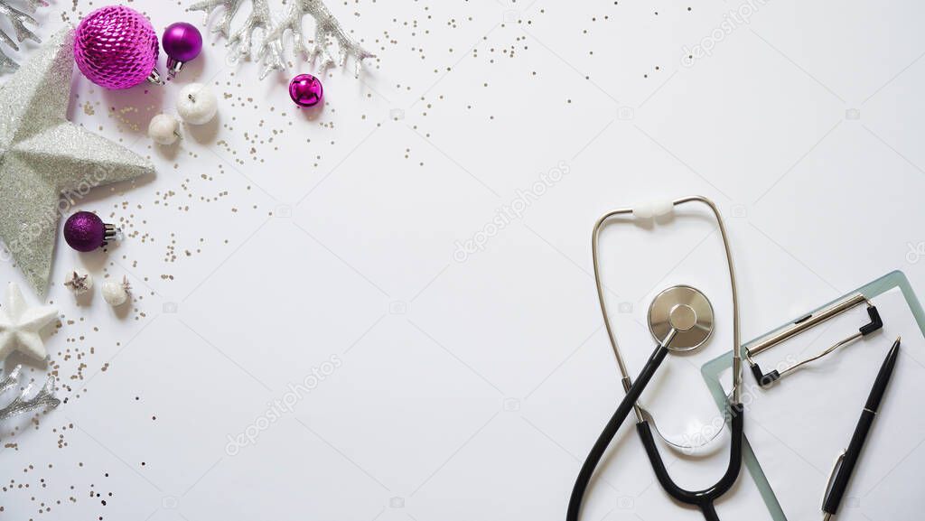 Christmas medical banner christmas decor white stars, purple balls, snowflakes, stethoscope and tablet on white background top view. Copyspace. Medicine new year flatly. Doctor writes down the text.