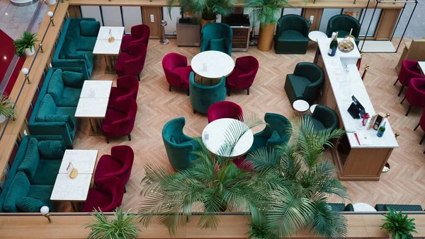 Empty restaurant with bright burgundy and green chairs, large living plants in flowerpots in a shopping center during the coronavirus epidemic, top view.Cozy modern interior of a restaurant, cafe.