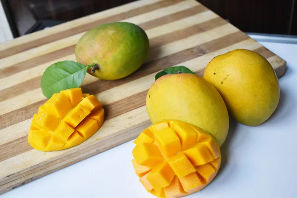Mangoes sliced in cubes on a wooden cutting board with green leaf