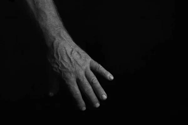 A man\'s, manly hand against a black background. The photo is in a low key. Horizontal